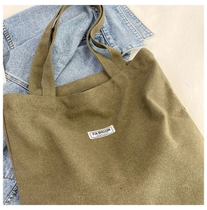 Detail of army green canvas tote bag with small white woven label and sturdy carry handles