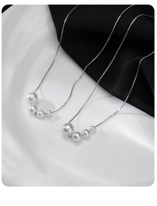 Detailed macro view of a silver necklace with four gradient white pearls on dark fabric