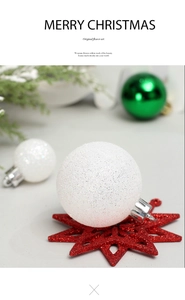Detailed view of white glitter Christmas ball ornament on red star base with tree greenery