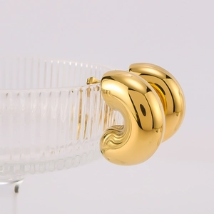 Polished 18K gold plated C-shaped chubby hoop earrings displayed on a glass rim