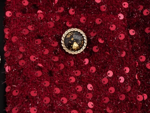 Dettaglio macro del tessuto tweed a paillettes rosse con bottone decorativo dorato