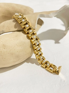 Macro detail of 18K gold-plated watch-link bracelet with elegant white pearl inlays