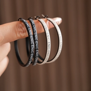 Détail des créoles en cuir noir et blanc avec des motifs de lettres ENIC élégants