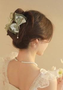 Close-up of elegant green bow hair claw clip with lace edges and a pearl tassel detail