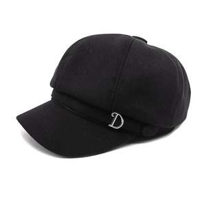 Close-up of black newsboy cap featuring a decorative silver metal letter D logo detail