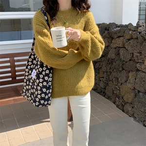 Detail of ginger yellow knitted sweater paired with a floral tote bag in a cafe setting