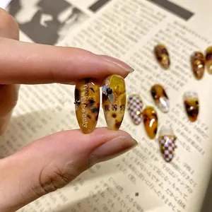 Amber style nail stickers with checkerboard patterns and pearl accents on fingers