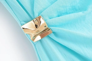 Détail macro d'une boucle en métal doré sur un tissu plissé de couleur cyan