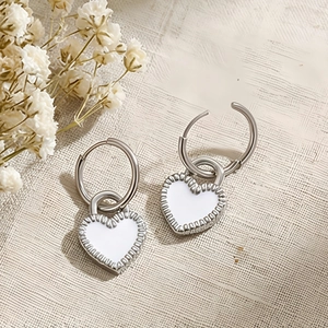 Detail of silver heart hoop earrings with white enamel finish and floral background