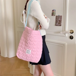 Pink heart-quilted tote bag with light blue straps and brand label shown on model