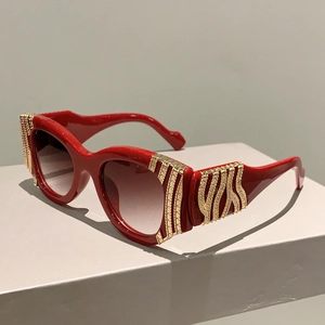 Detailed view of red cat-eye sunglasses with gold metal decorative temple patterns