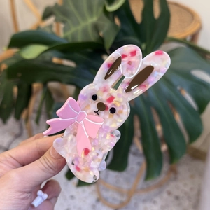 Detailed view of pink acetate rabbit hair clip with glitter and ribbon held in hand
