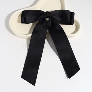 Close-up of elegant black satin bow hair clip with long ribbon on a ceramic plate