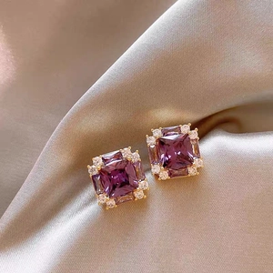 Macro shot of vintage style square purple zircon earrings on champagne silk background