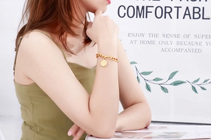 Close-up of gold chain bracelet with a tree of life coin pendant on a female wrist