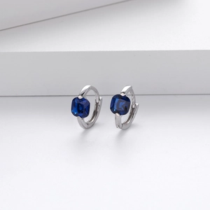 Detail of silver S925 earrings featuring square blue zircon stones on white display