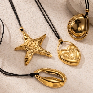 Detail of gold starfish and heart pendants on black cords over stone background