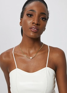 Close-up of a gold Cuban chain necklace featuring a white freshwater pearl pendant on a model