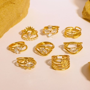 Gold stainless steel rings with zircon heart and flower designs on a textured rock surface