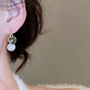 Détail de la boucle d'oreille cœur et perle portée à l'oreille, serti doré