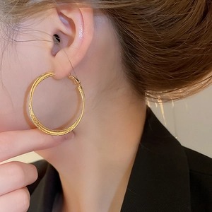 Macro side view of model wearing large 18k gold-plated double-layer crossover hoop earrings