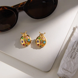 Detail shot of golden ladybug earrings with colorful rhinestones on a silver laptop
