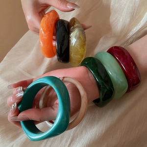 Detail showing various colorful marble pattern resin acrylic wide bangles on a model's wrist