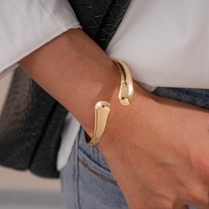 Minimalist irregular gold open bangle with polished teardrop ends on a woman wrist