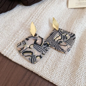 Close-up of geometric square earrings with marble texture and gold diamond metal connector