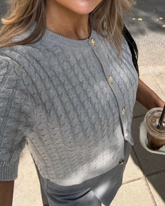 Detail of grey cable knit short sleeve cardigan featuring embossed gold buttons