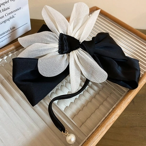 Detail of elegant black satin bow hair clip with white tulle flower and pearl pendant