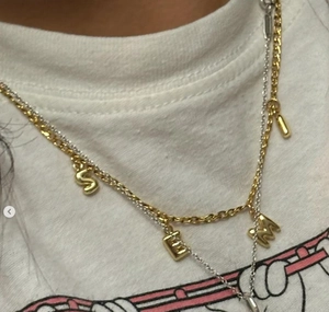 Gros plan sur collier double couche avec lettres bulles S E M en or 18k et chaîne argent