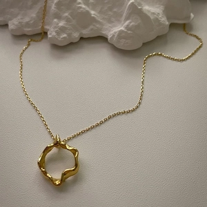 Detailed close-up of a minimalist gold wavy ring pendant on a fine cross chain necklace