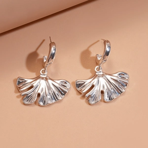 Detailed close-up of silver ginkgo leaf earrings with zircon crystals on a beige background