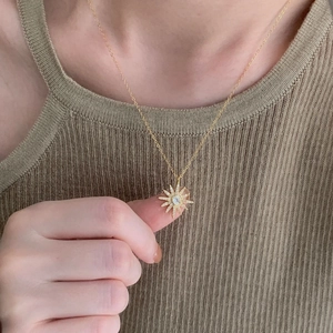 Close-up of a gold sunburst star pendant necklace with sparkling zircon on a model's hand