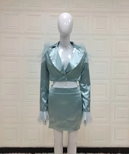 Détail d'un ensemble en satin avec blazer et jupe orné de plumes aux épaules et poignets