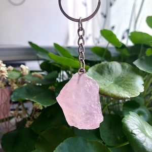 Natural pink crystal raw stone keychain with silver metal chain on a leaf background