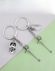 Macro detail of silver fencing mask and sword charms on a polished metal keychain