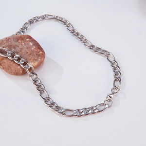Close-up of a silver Figaro chain necklace with a lobster clasp next to a decorative stone