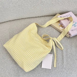 Detail of yellow gingham canvas tote bag with knotted strap on soft textured background