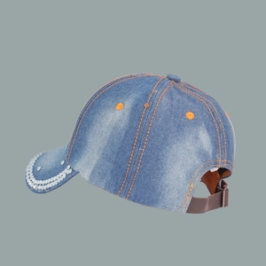 Detail of blue denim baseball cap showing orange stitching and white pearl rim ornaments
