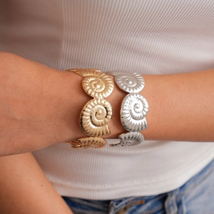 Detailed close-up of gold and silver open bracelets featuring spiral seashell relief texture