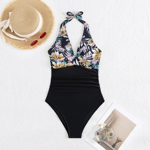 Flat lay of a floral halter neck swimsuit with black ruched waist and holiday accessories