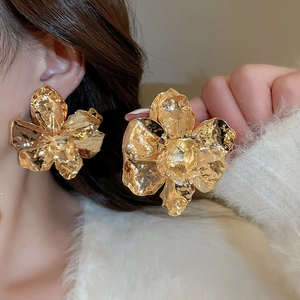 Macro shot of large golden metal flower earring with irregular hammered texture on model