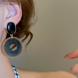 Primo piano di orecchini pendenti tondi intrecciati neri e oro su modella in stile retrò