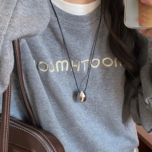 Detail view of oval silver metal pendant with black leather cord on a grey hoodie
