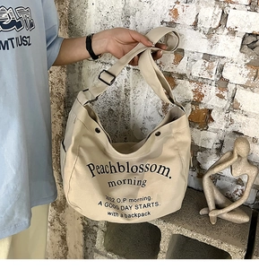 Détail d'un sac cabas en toile beige avec imprimé lettres noires et bandoulière réglable