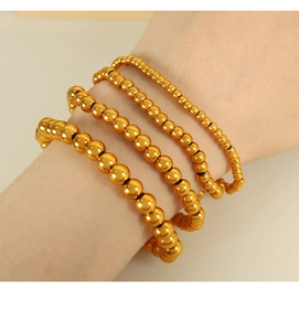 Detail of four layered gold bead bracelets in various sizes on a woman's wrist