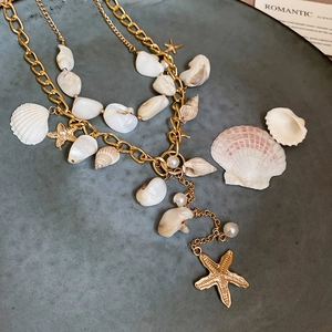 Detail of layered gold ocean necklace with starfish, shells, and pearls on a grey plate