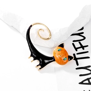Close-up of enamel cat brooch with orange face, green gemstone eyes and golden tail
